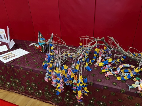 A table inside the school draped with a branch holding many colorful origami cranes